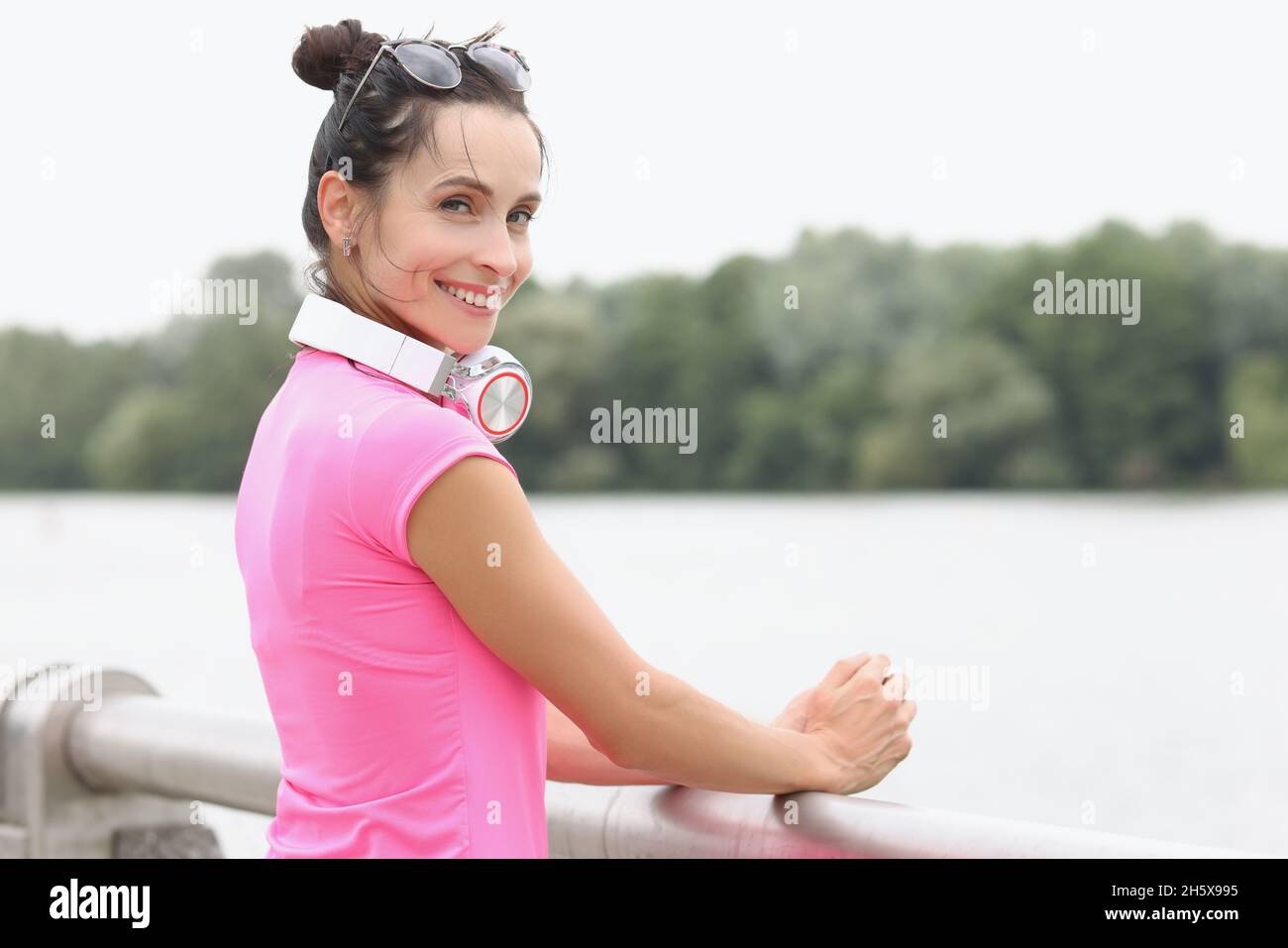 Jeune femme souriante avec un casque sur le cou, debout sur le pont Banque D'Images