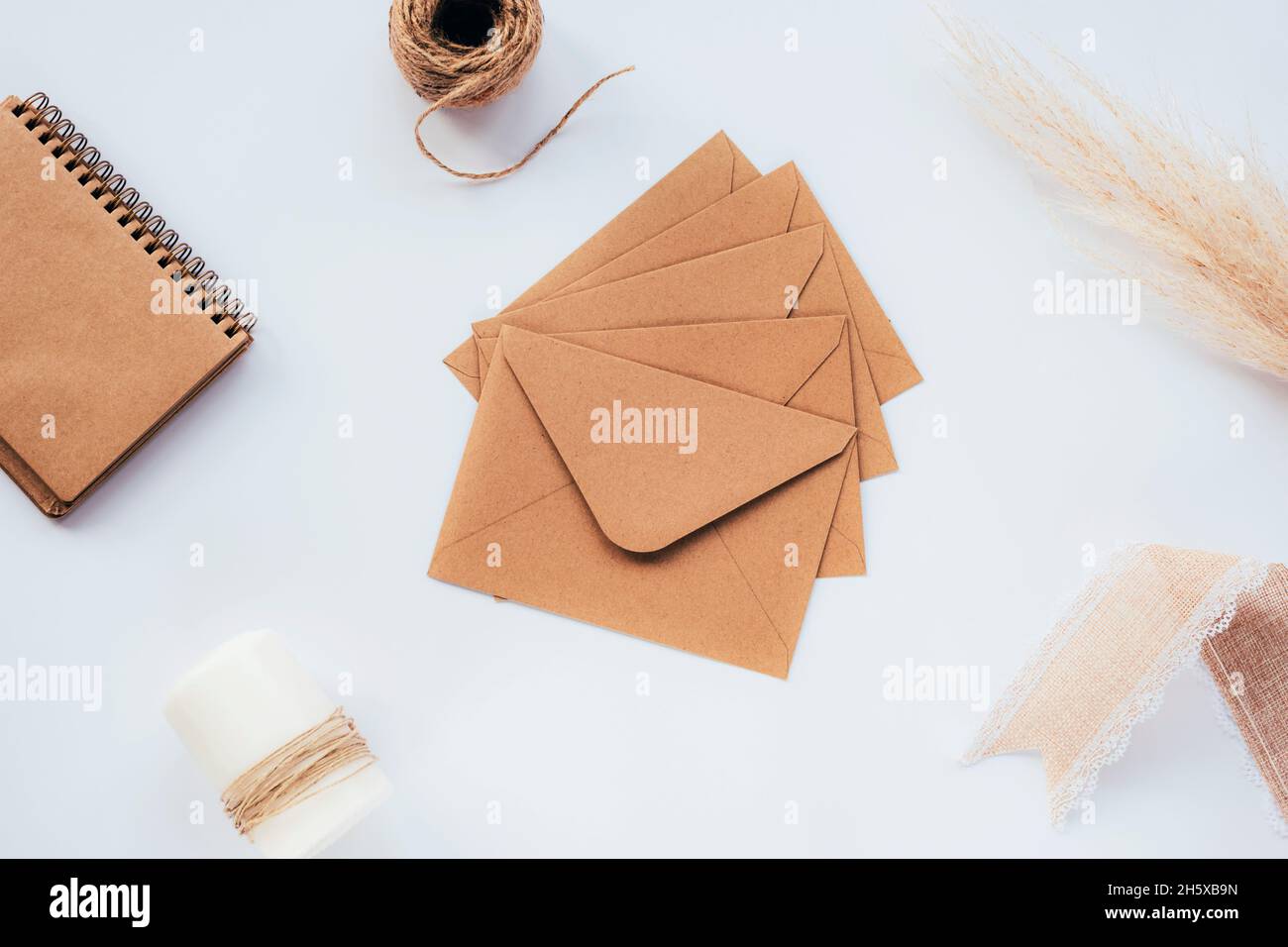 Enveloppes brunes vierges sur la table blanche avec bloc-notes, bougie, ficelle, ruban d'artisanat et pampas d'herbe.Vue de dessus, plan d'appartement Banque D'Images