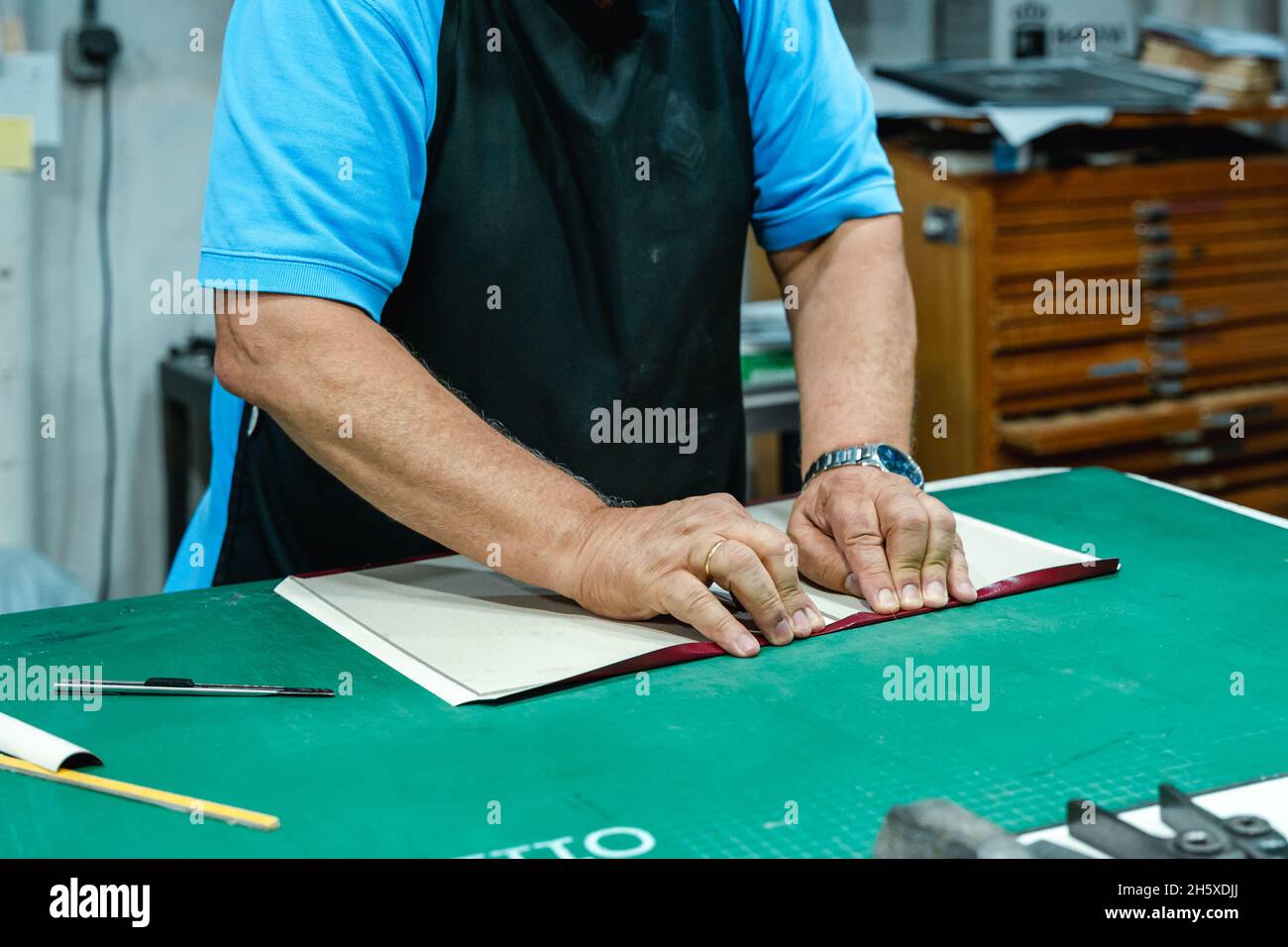 Cachez un artisan masculin méconnu dans des vêtements décontractés et une couverture pliante de tablier de l'album tout en vous tenant debout à l'établi dans un studio d'impression traditionnel Banque D'Images