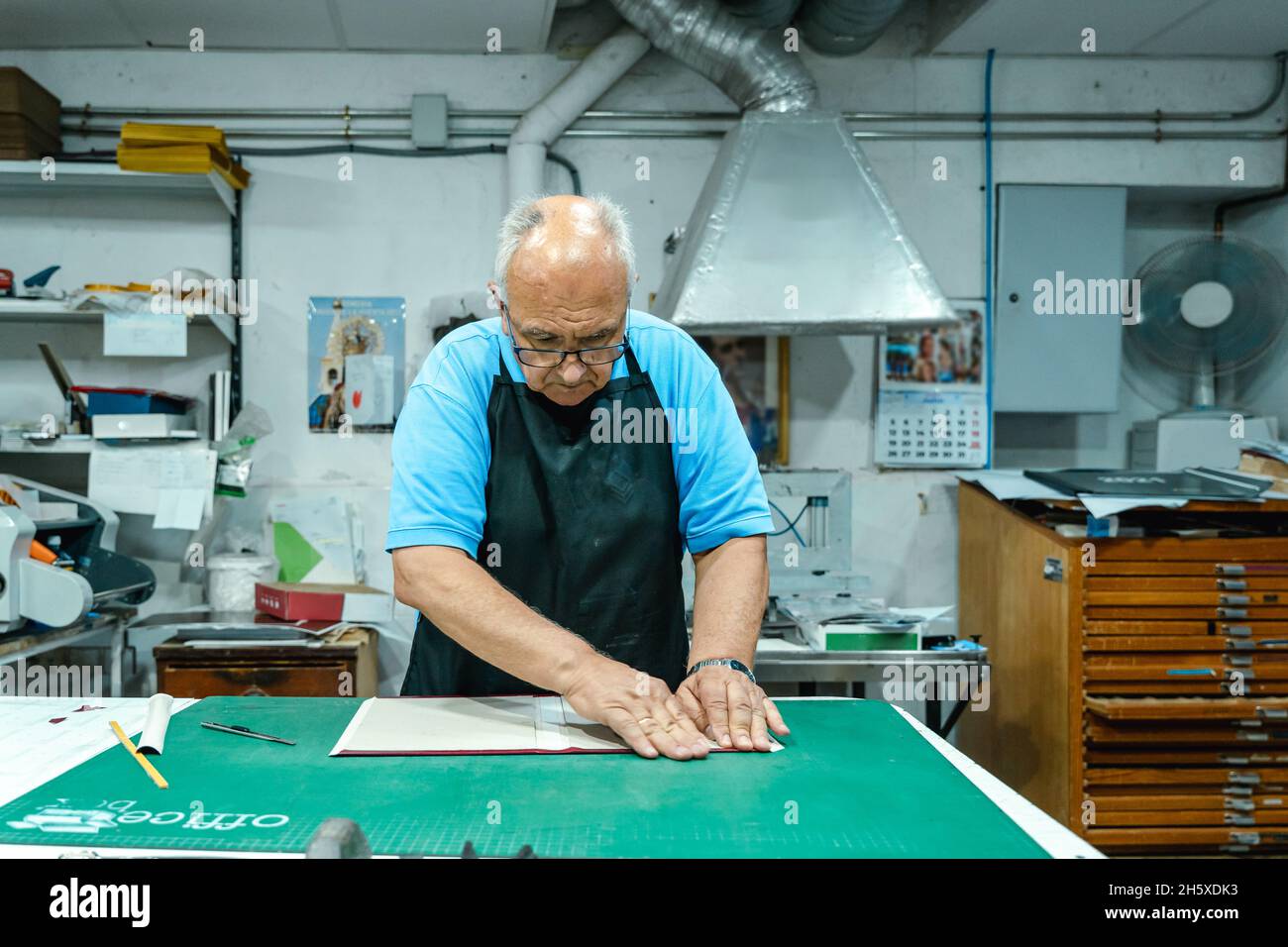 Cachez un artisan masculin méconnu dans des vêtements décontractés et une couverture pliante de tablier de l'album tout en vous tenant debout à l'établi dans un studio d'impression traditionnel Banque D'Images