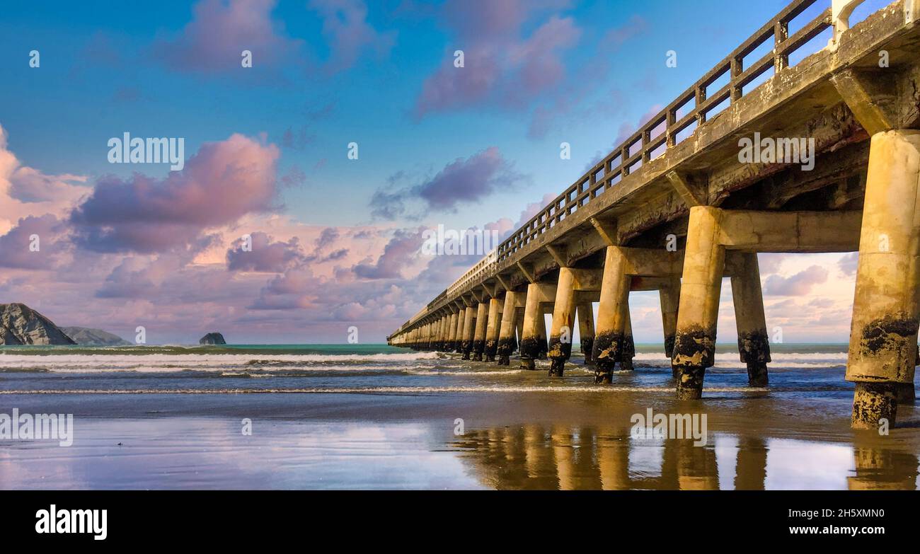 Le quai en bois historique de Tolaga Bay, lors d'une journée magnifique avec des reflets sur le sable humide Banque D'Images