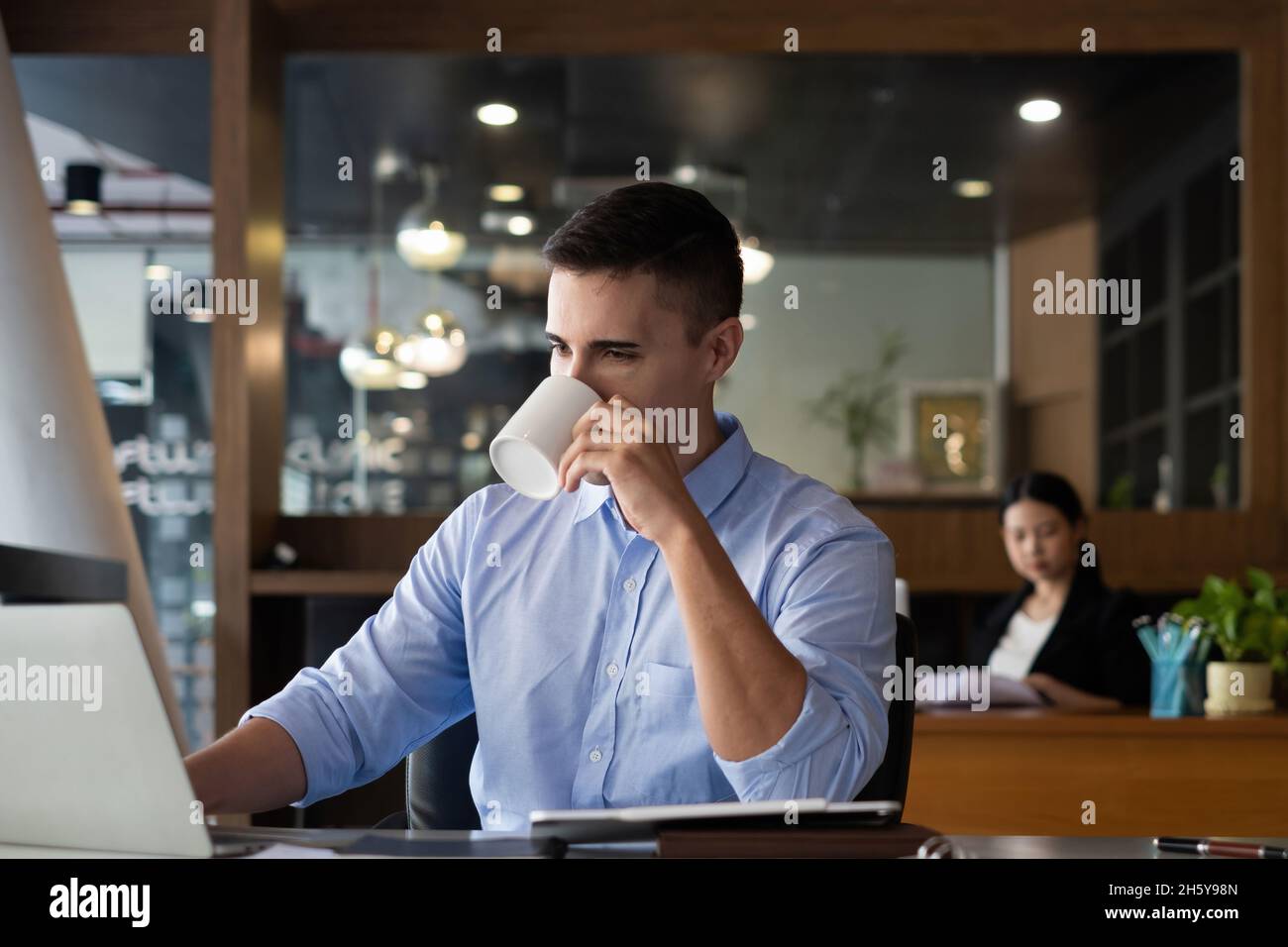 Un homme d'affaires buvant du café le matin avec un partenaire d'affaires travaillant à l'arrière-plan au bureau. Banque D'Images