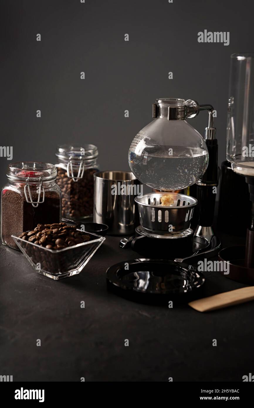 Machine à café à aspiration également connue sous le nom de cafetière aspirateur, siphon ou syphon et grains de café grillés sur table en pierre noire rustique.Copiez l'espace pour votre tex Banque D'Images