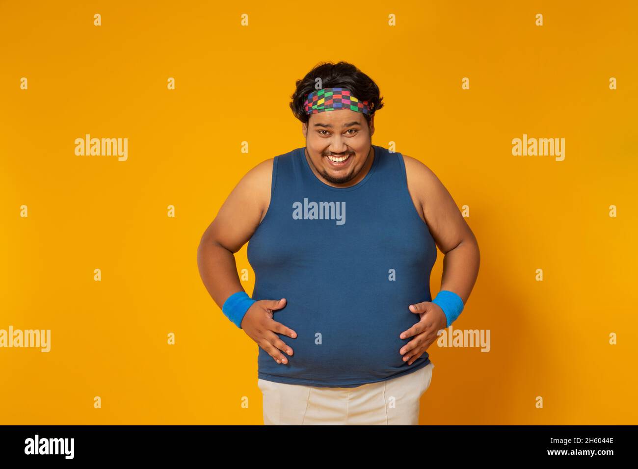Portrait d'un gros homme souriant tout en plaçant les mains sur le ventre contre un fond plat. Banque D'Images