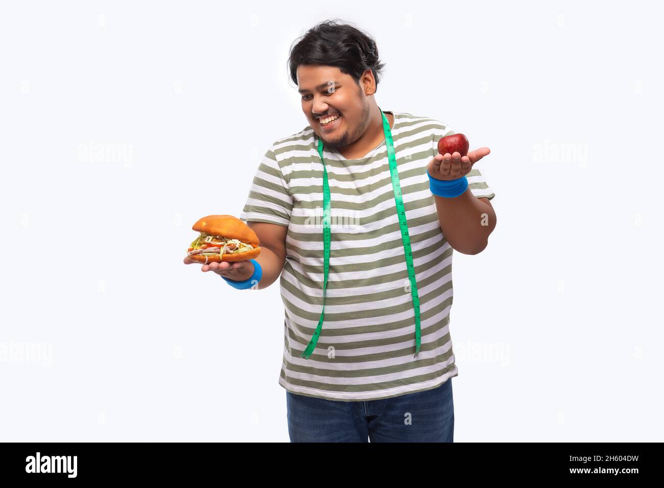 Portrait d'un gros homme avec du ruban de mesure autour de son cou dévorant un hamburger plutôt qu'une pomme. Banque D'Images