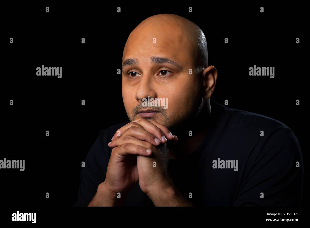 Portrait d'un homme chauve regardant avec un regard tendu anxieux sur fond noir foncé. Banque D'Images