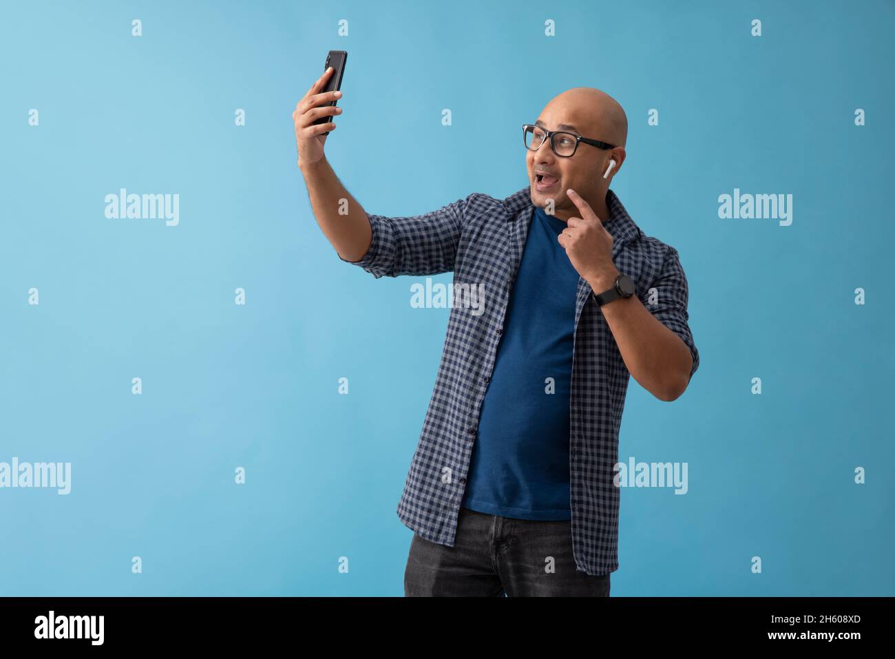 Portrait d'un homme chauve avec bluetooth dans ses oreilles appels vidéo sur téléphone mobile. Banque D'Images