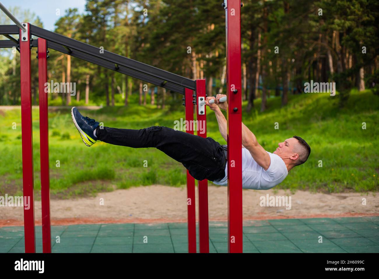 Homme caucasien faisant une planche de dos sur les barres inégales. Entraînez-vous sur le terrain de sport. Banque D'Images