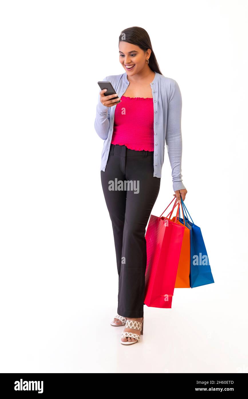 Jeune fille indienne regardant un smartphone tout en tenant des sacs d'achats dans sa main Banque D'Images