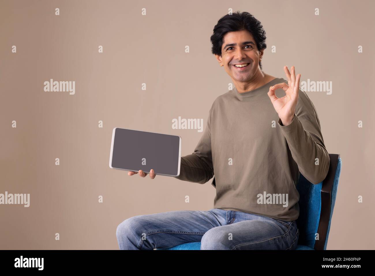 Homme indien montrant sa satisfaction à l'égard de la tablette tout en étant assis sur une chaise Banque D'Images