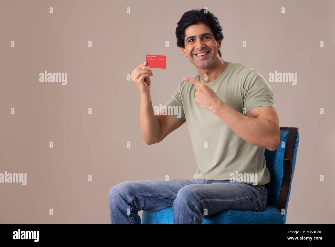 Homme indien montrant sa carte de crédit en étant assis sur une chaise Banque D'Images