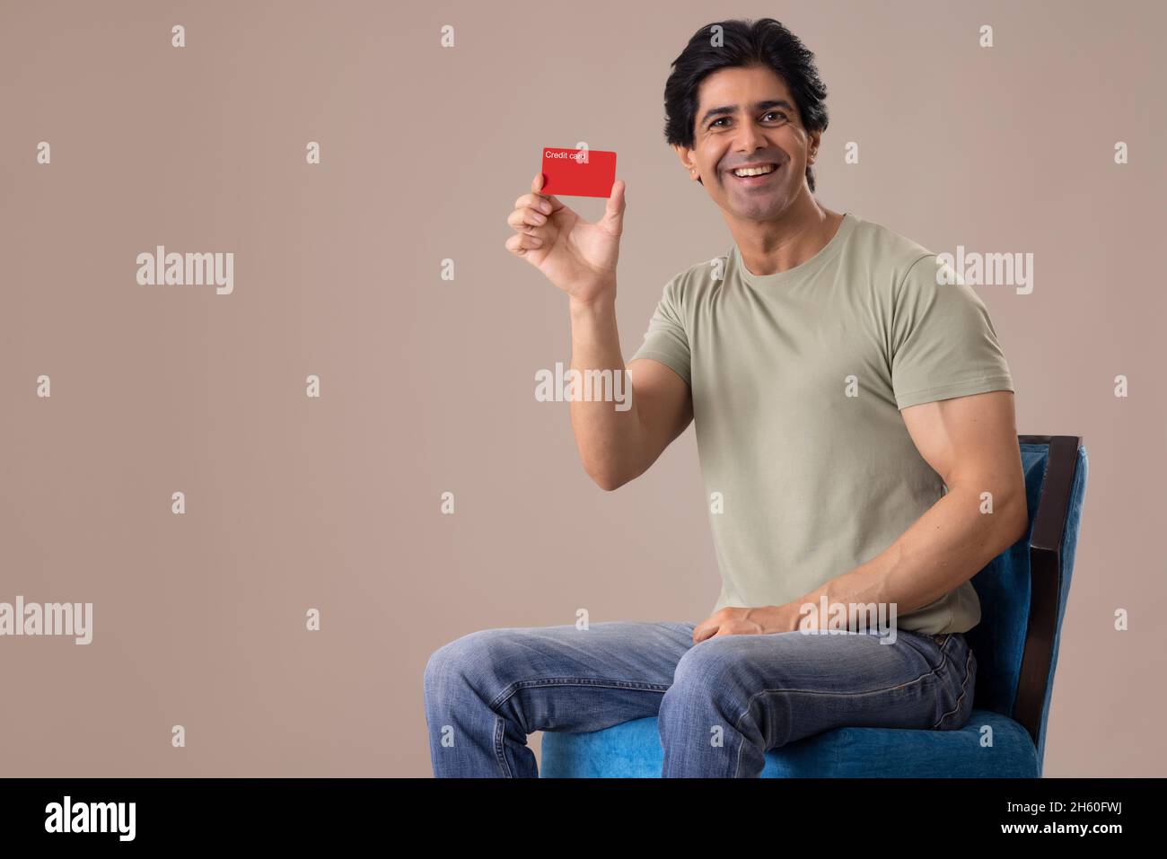 Homme indien montrant sa carte de crédit en étant assis sur une chaise Banque D'Images