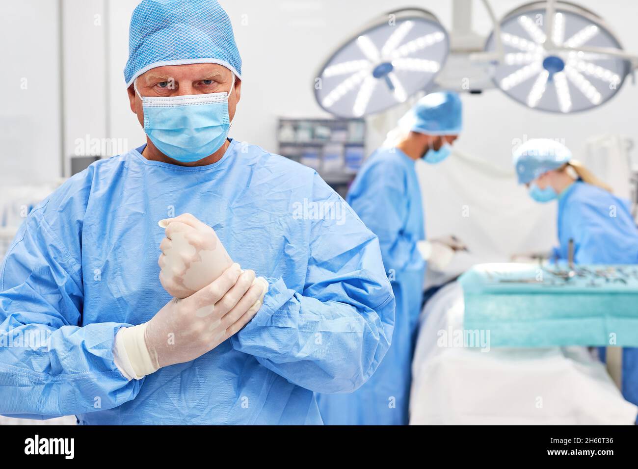 Chirurgien compétent dans des vêtements de protection avant une opération avec l'équipe de chirurgie en arrière-plan Banque D'Images