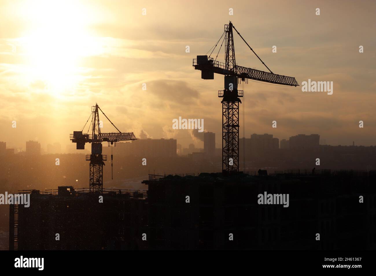 Silhouettes de grues de construction et de bâtiments résidentiels non finis sur fond de lever de soleil. Construction de logements, immeuble en ville Banque D'Images