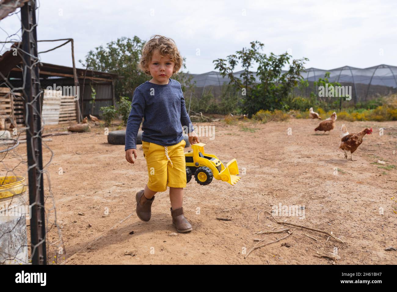 Portrait en longueur d'un garçon mignon tenant un jouet bulldozer tout en marchant à l'extérieur du stylo à la ferme Banque D'Images