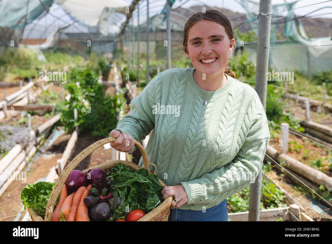 Portrait d'une jeune agricultrice souriante tenant des légumes fraîchement récoltés dans un panier à la ferme Banque D'Images