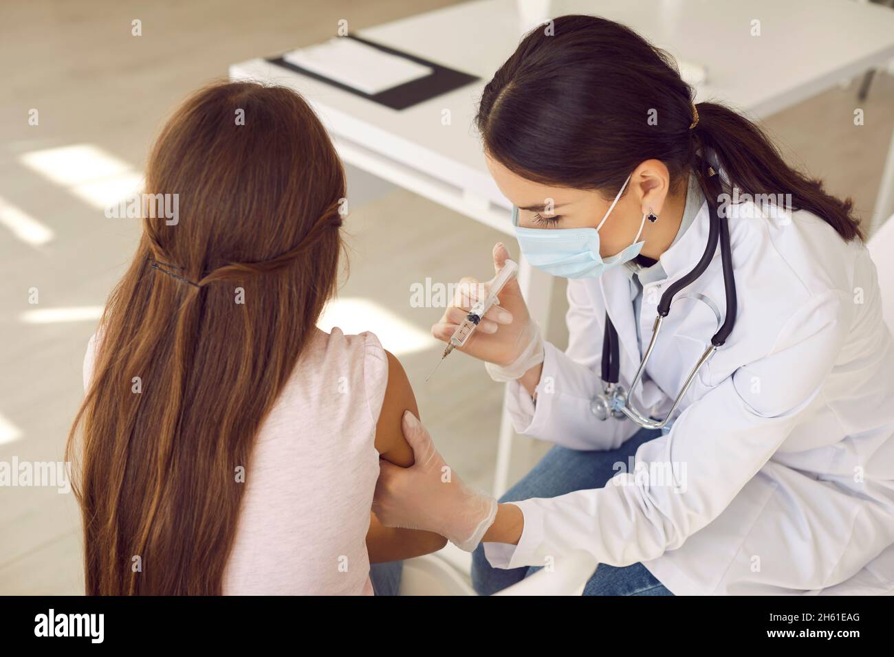 La femme médecin en masque de protection injecte le vaccin contre Covid 19 à une adolescente inconnue. Banque D'Images