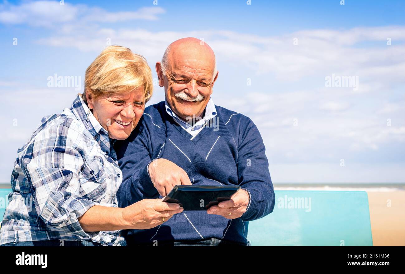 Couple heureux senior s'amuser avec une tablette à la plage - Portrait de l'homme et de la femme en interaction avec la technologie moderne Banque D'Images