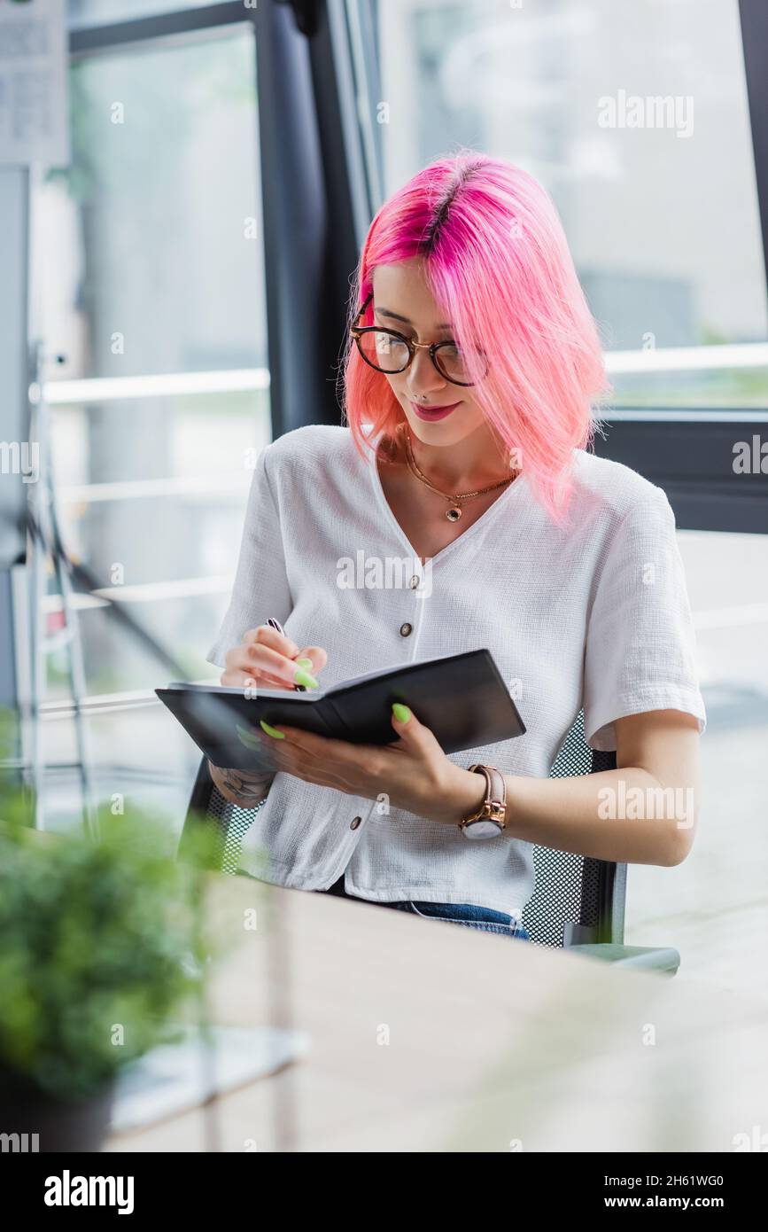femme d'affaires tatouée avec des cheveux roses écrivant sur le carnet Banque D'Images