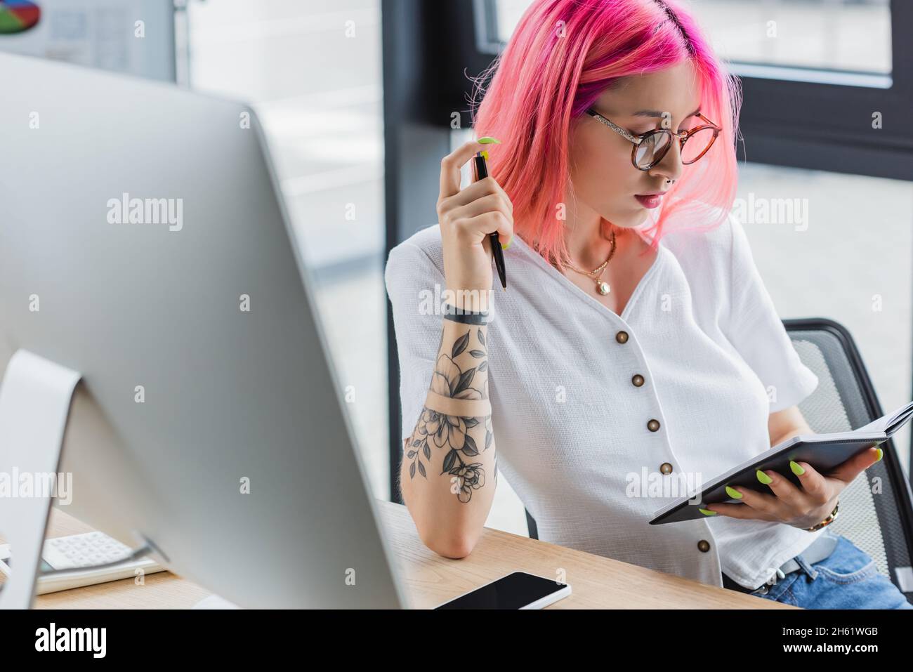 femme d'affaires tatouée avec un stylo et un carnet à cheveux roses Banque D'Images