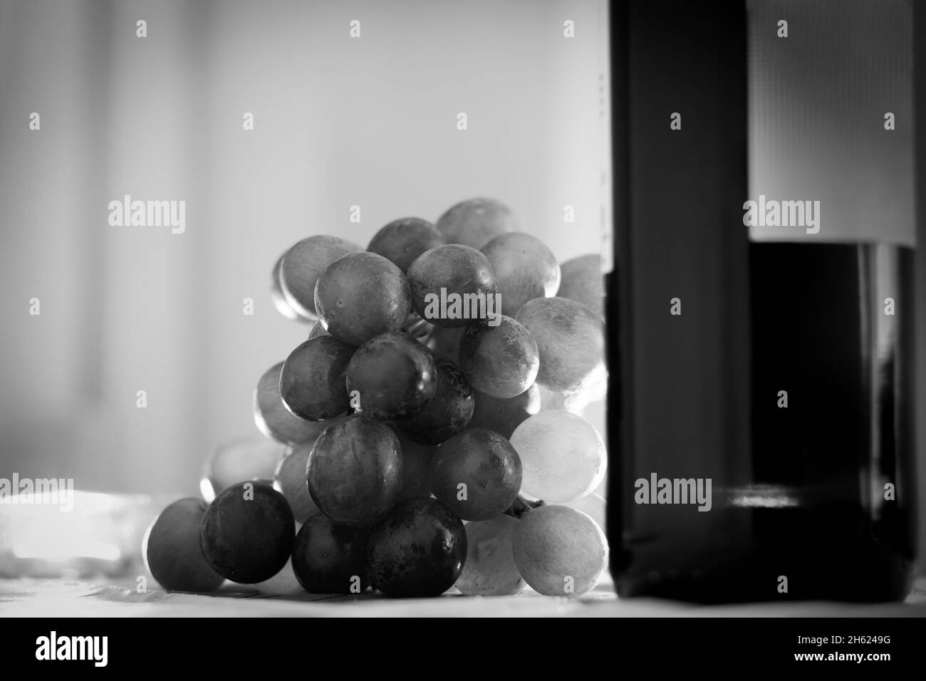 Raisins et bougies illuminées par une bouteille de vin sur la table. Photographie en noir et blanc Banque D'Images