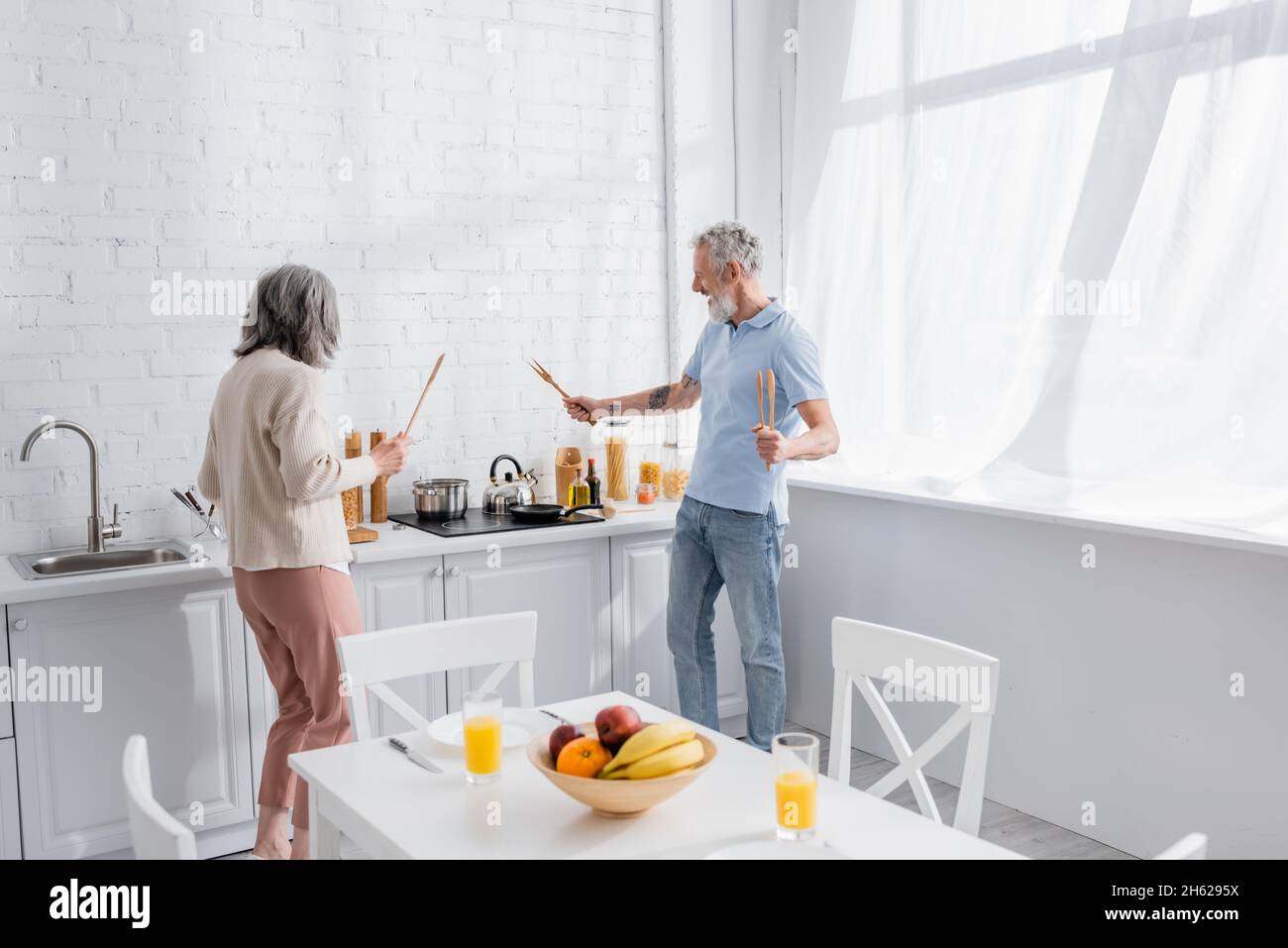 Couple d'âge mûr et gai tenant des spatules près du plan de travail dans la cuisine Banque D'Images