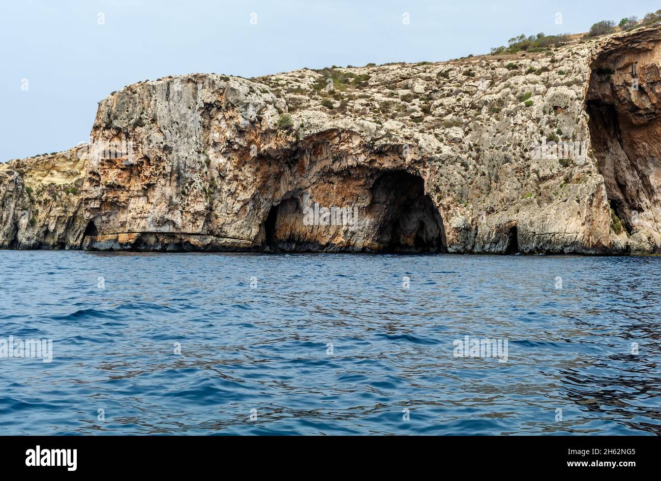 Les bords rocailleux de la Grotte bleue, Malte, s'en sortant de la mer Méditerranée et éclairé par le soleil du matin.Formations rocheuses avec grottes. Banque D'Images