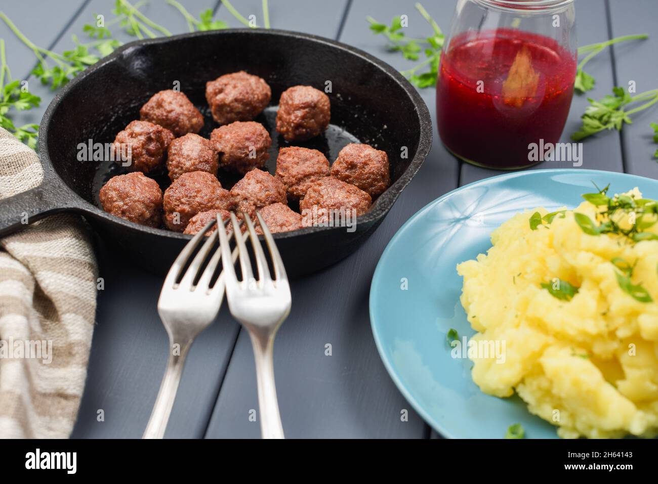 Boulettes de viande de Suède faites maison dans une poêle en fonte, servies  avec une purée de pommes de terre et une sauce aux baies rouges avec deux  fourchettes vue de côté