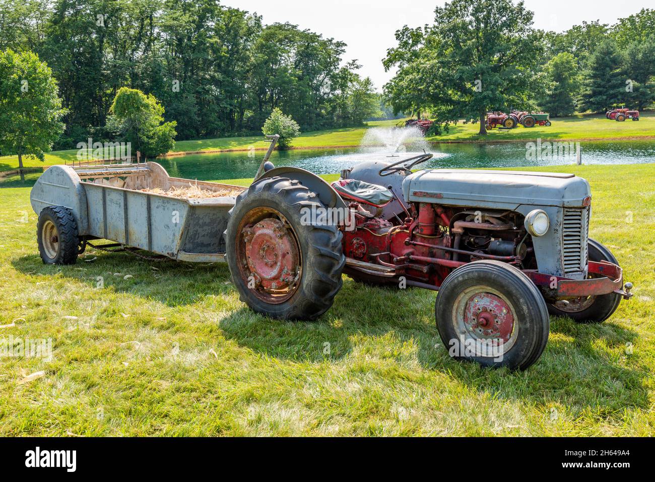 Un ancien tracteur agricole Massey Ferguson 35 rouge et gris avec épandeur de fumier est exposé