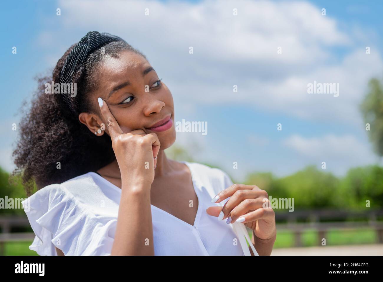 Belle femme avec son doigt sur son temple en regardant loin dans le parc Banque D'Images