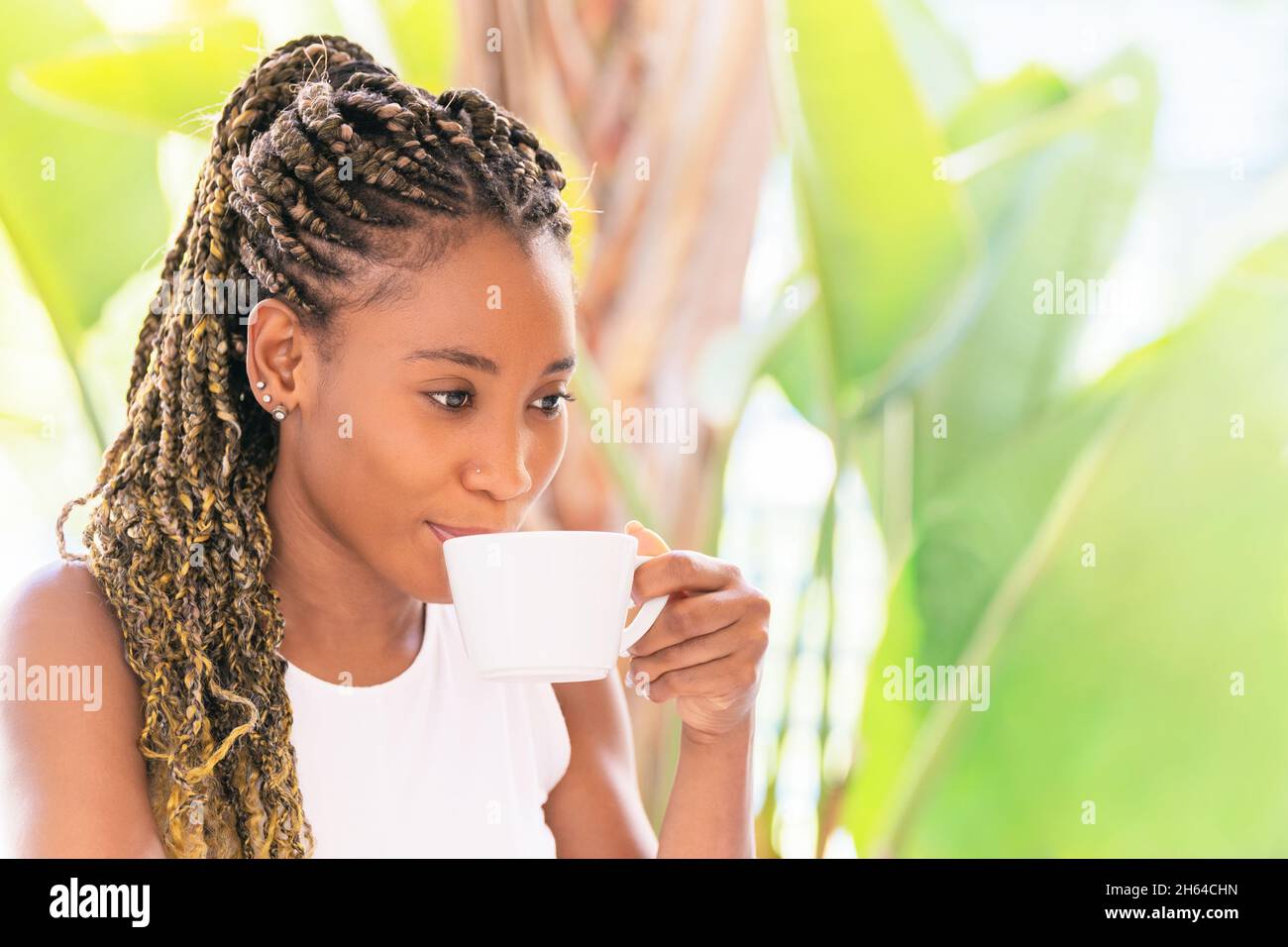 Une femme afro-américaine boit une tasse de café tout en regardant vers l'extérieur Banque D'Images