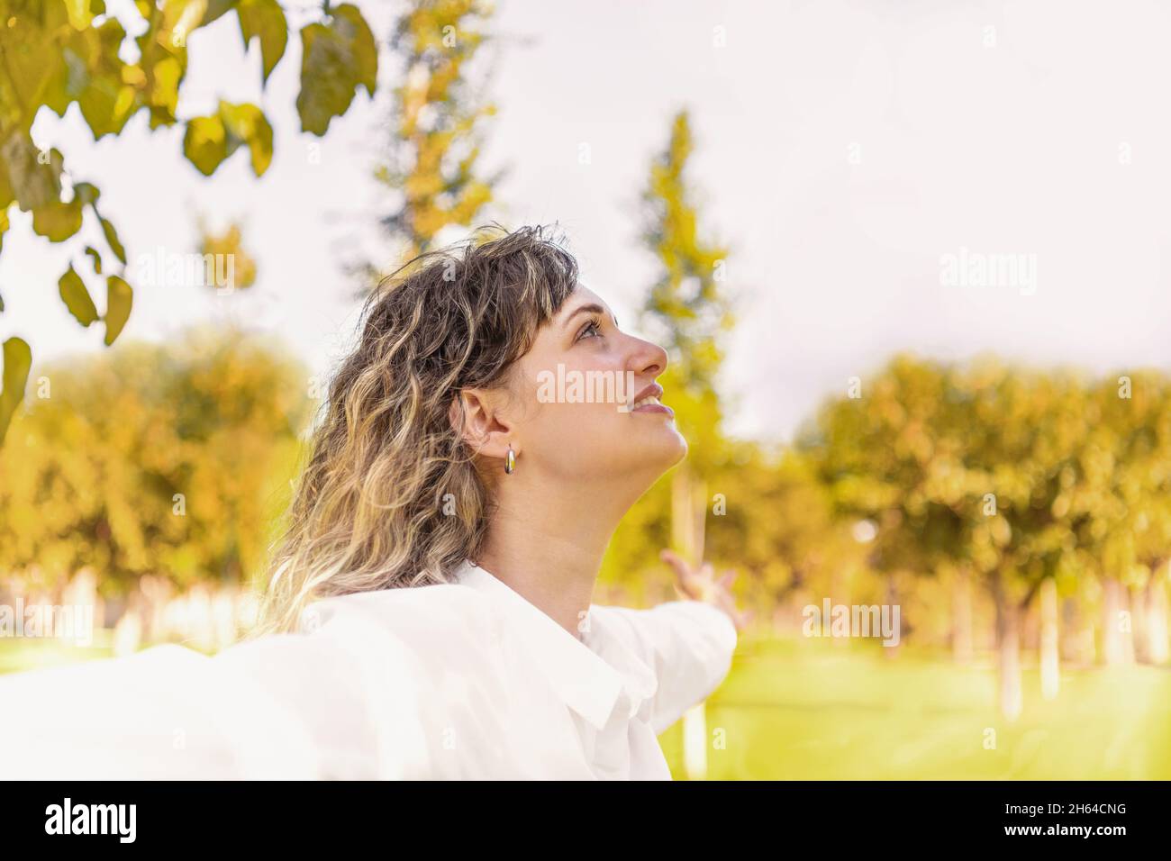 Profil d'une femme blonde levant les bras à l'extérieur Banque D'Images