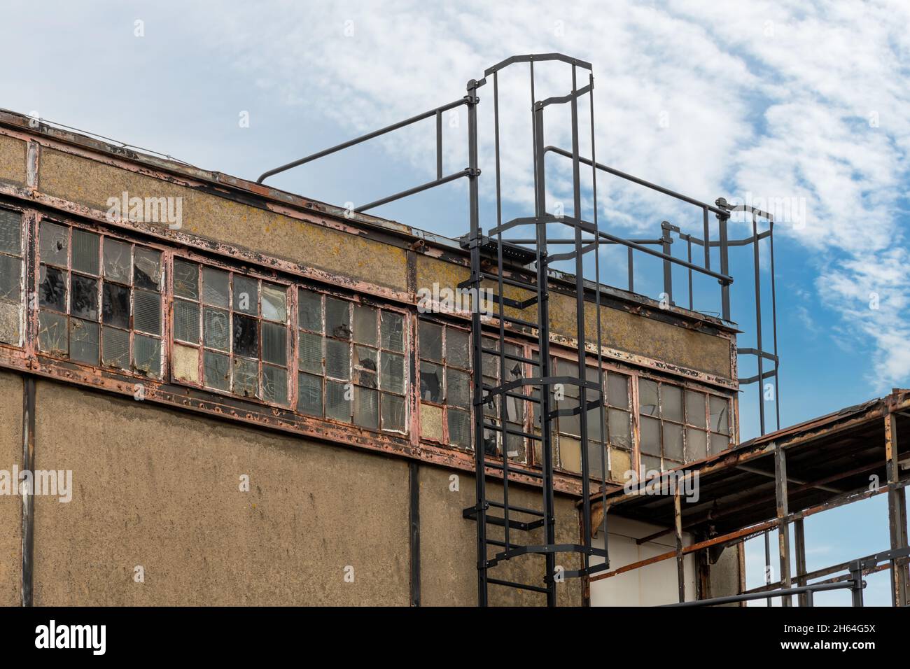 Vue partielle de la façade de l'usine en ruine avec échelle d'évacuation en fer avec cage menant au toit; mur et fenêtres sales Banque D'Images