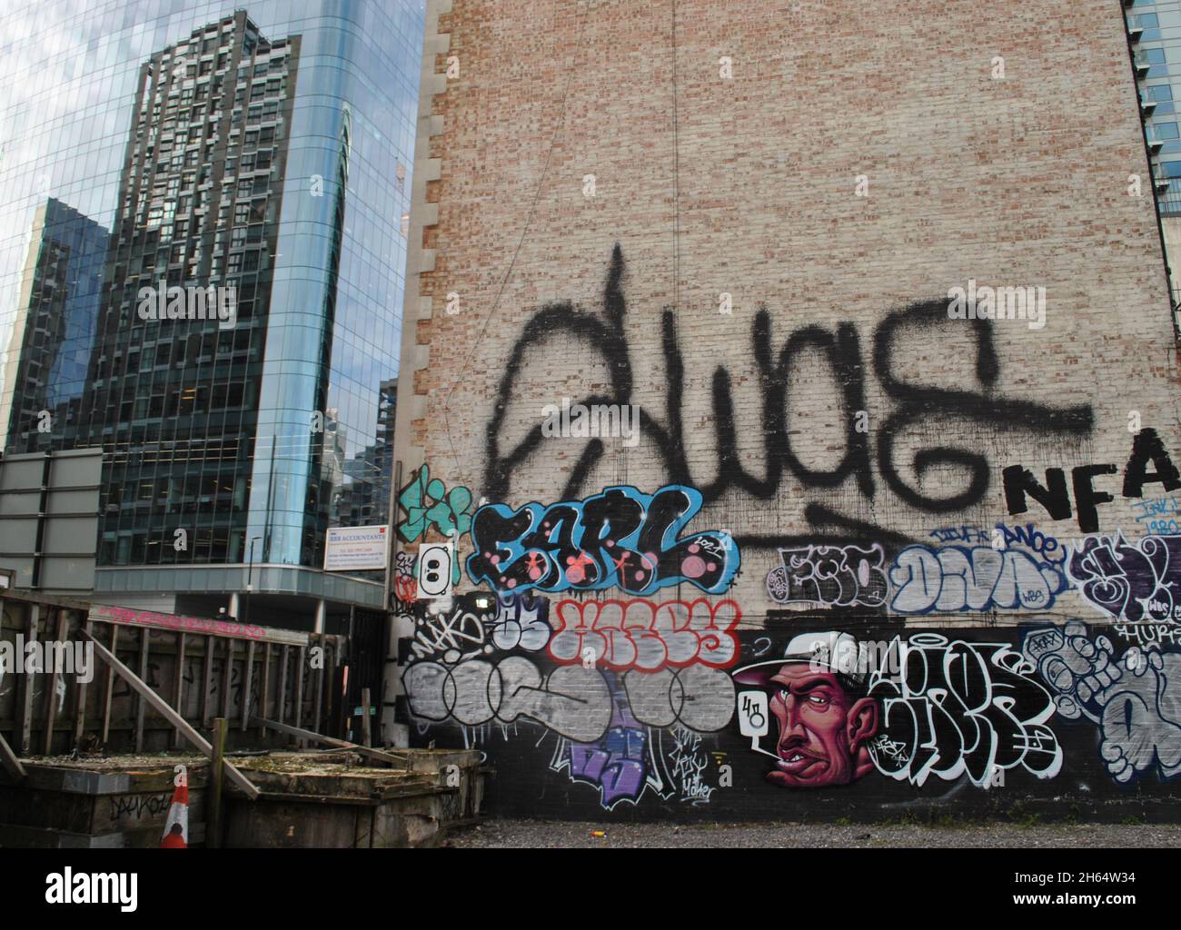 Un mur de graffiti à Whitechapel, dans l'est de Londres avec le personnage de l'artiste de rue Gent48 et d'autres étiquettes graffiti avec de nouveaux bâtiments en verre en arrière-plan. Banque D'Images