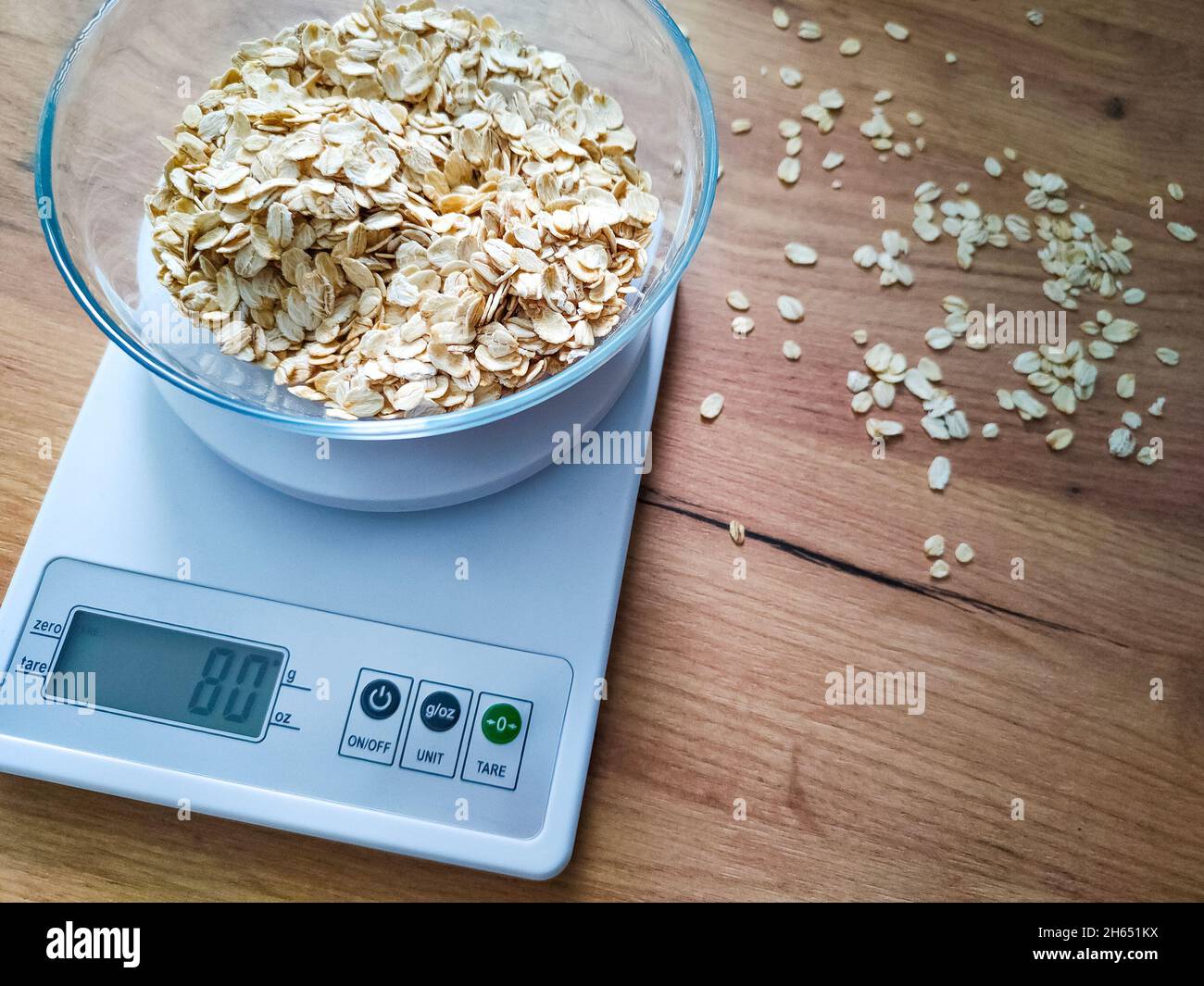 Gruaux d'avoine, gruaux pesant dans un bol en verre sur des balances électroniques de cuisine sur une table en bois. Banque D'Images