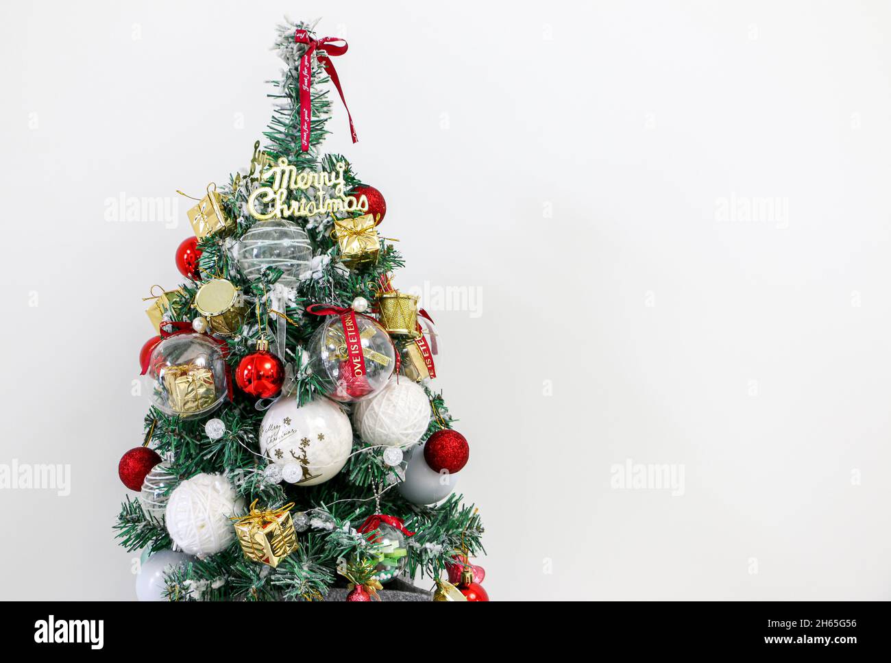 Arbre de Noël décoré avec un message de Noël joyeux, des boules rouges et blanches, des cloches rouges, des cadeaux dorés et des tambours dorés Banque D'Images