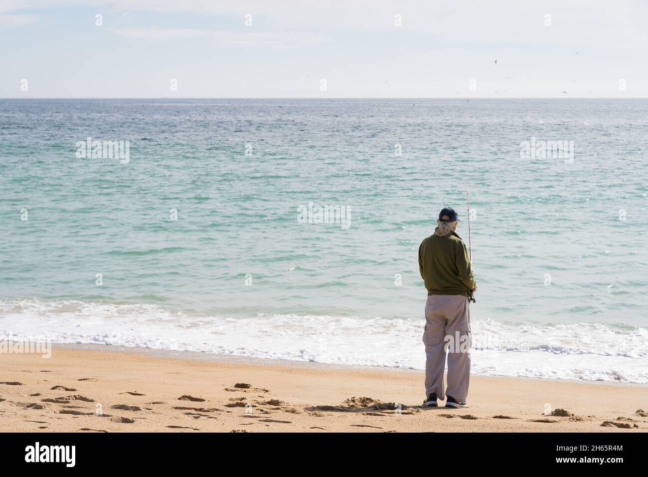 Arrière de l'homme solitaire senior pêche sur la plage.Personne aînée anonyme tenant la barre au bord de la mer.Concept de joie de retraite Banque D'Images