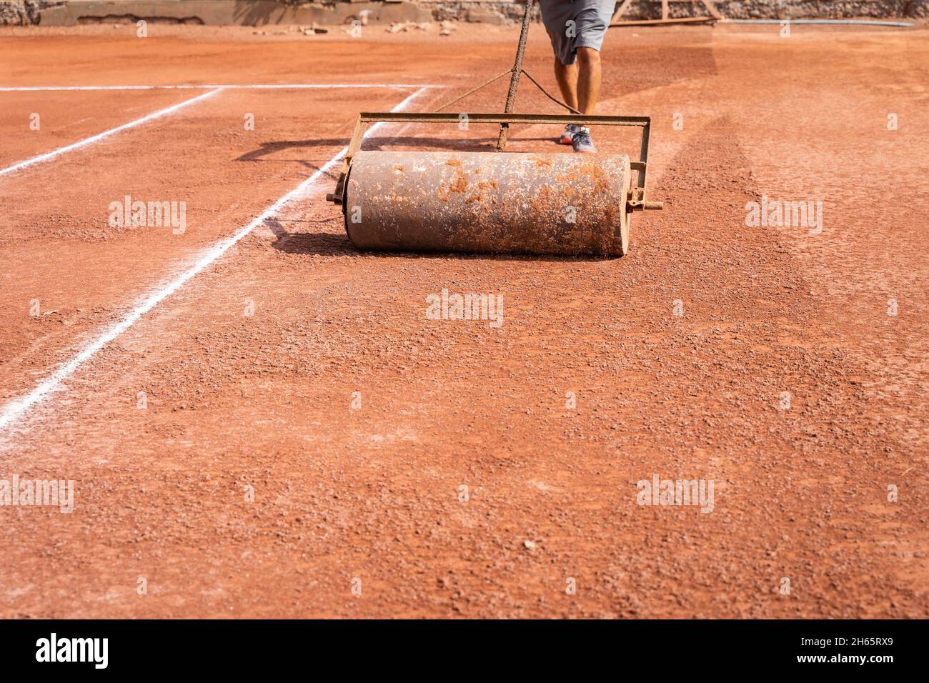 L'homme d'entretien fait le plein d'un court de tennis en terre battue avec un rouleau lourd le jour ensoleillé.Concept de tournoi de sport en plein air Banque D'Images