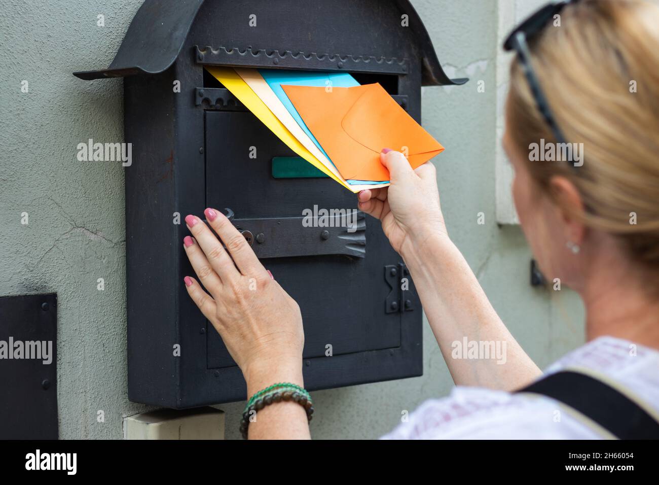 Le transporteur de courrier insère des lettres dans la boîte aux lettres.Femme porte des enveloppes colorées.Employé postal livrant la correspondance Banque D'Images