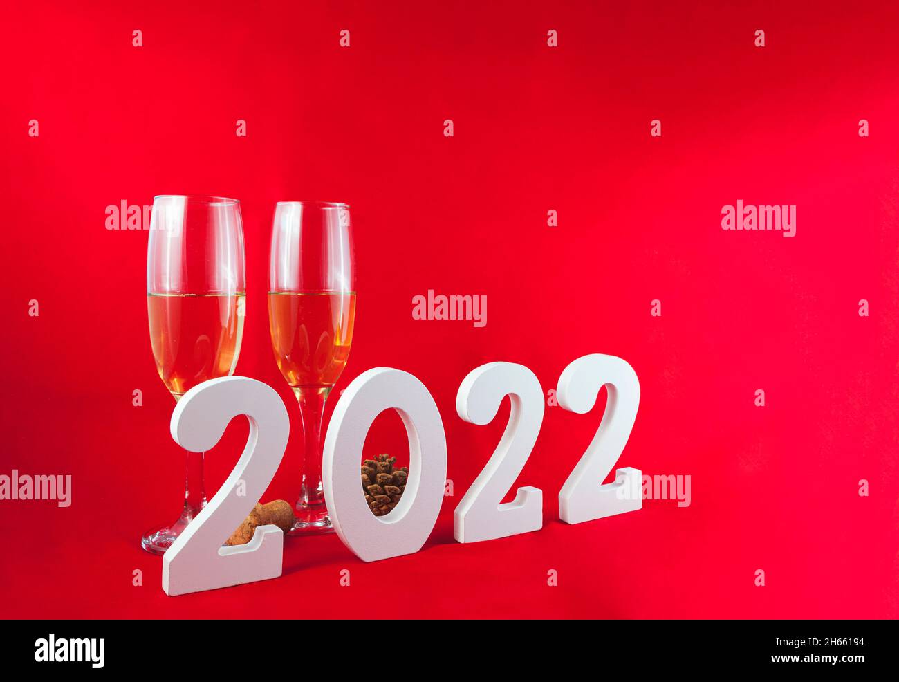 Sur fond rouge, il y a deux verres en cristal avec champagne, un cône de pin et un bouchon en liège.Devant elle se trouve le numéro 2022 en blanc. Banque D'Images