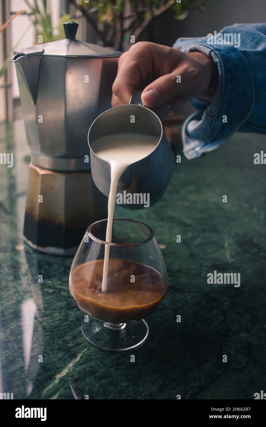 Modèle à main jeune tendance qui verse du lait pour préparer du café au lait Banque D'Images