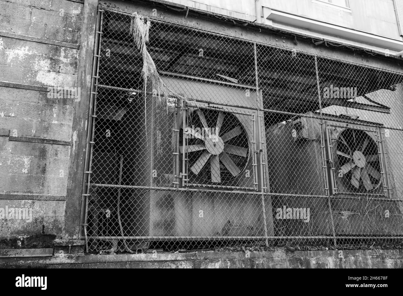 Ancien bâtiment industriel avec de grands ventilateurs et une clôture à maillons de chaîne Banque D'Images