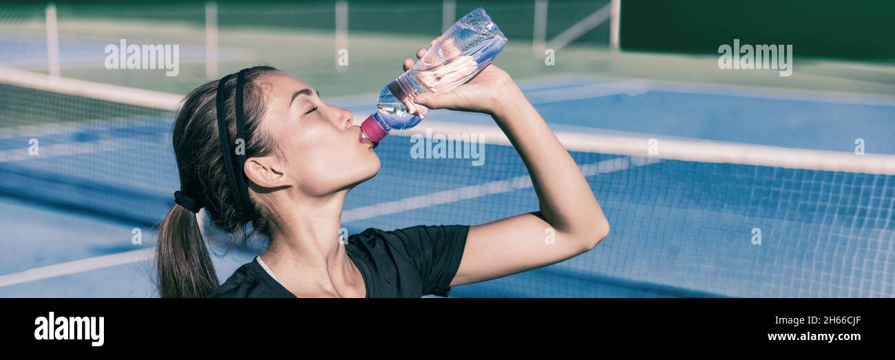 Thirsty Sporty Asian fille boire de l'eau tout en jouant au tennis sur le court extérieur.Sports active style de vie femme hydratant avec bouteille de sports nautiques Banque D'Images