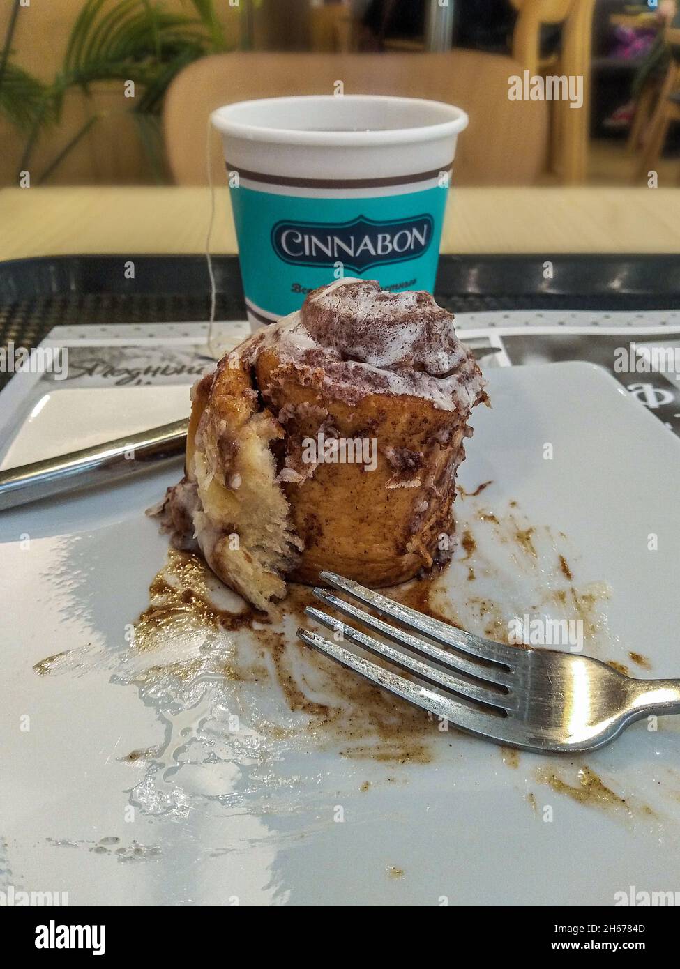 Saint-Pétersbourg, Russie - 21 juin 2021.Une tasse jetable avec le thé et le gâteau cinnabon a commencé et fini, fourchette et couteau, sur la table Banque D'Images