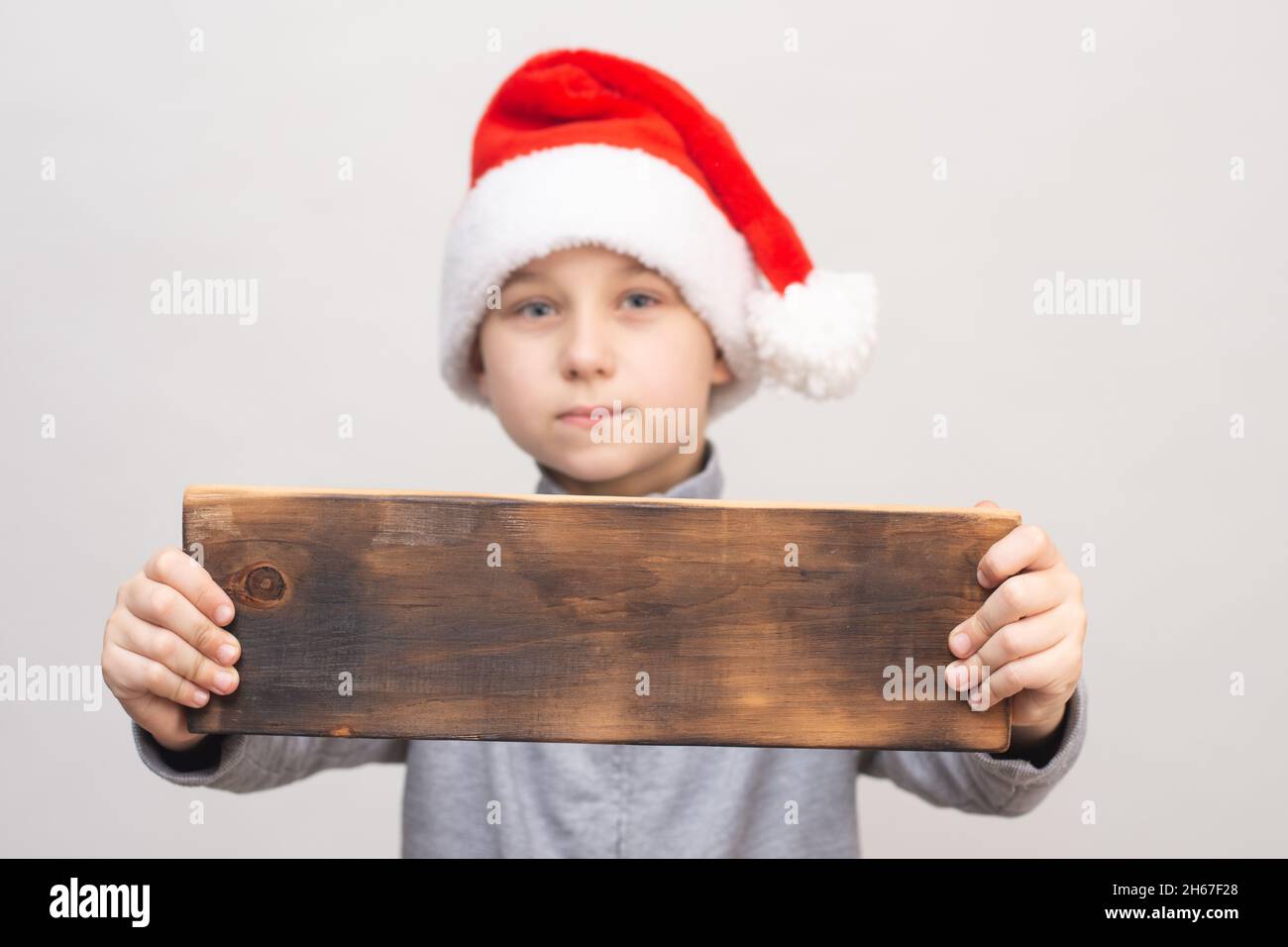 Un panneau en bois pour votre publicité ou texte dans les mains d'un garçon dans un chapeau de Père Noël. Banque D'Images