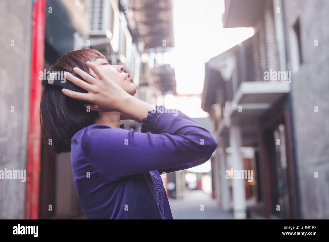 Bonne jeune femme asiatique à écouter de la musique avec des écouteurs dans la rue. Banque D'Images Bonne jeune femme asiatique à écouter de la musique avec des écouteurs dans la rue. Banque D'Images
