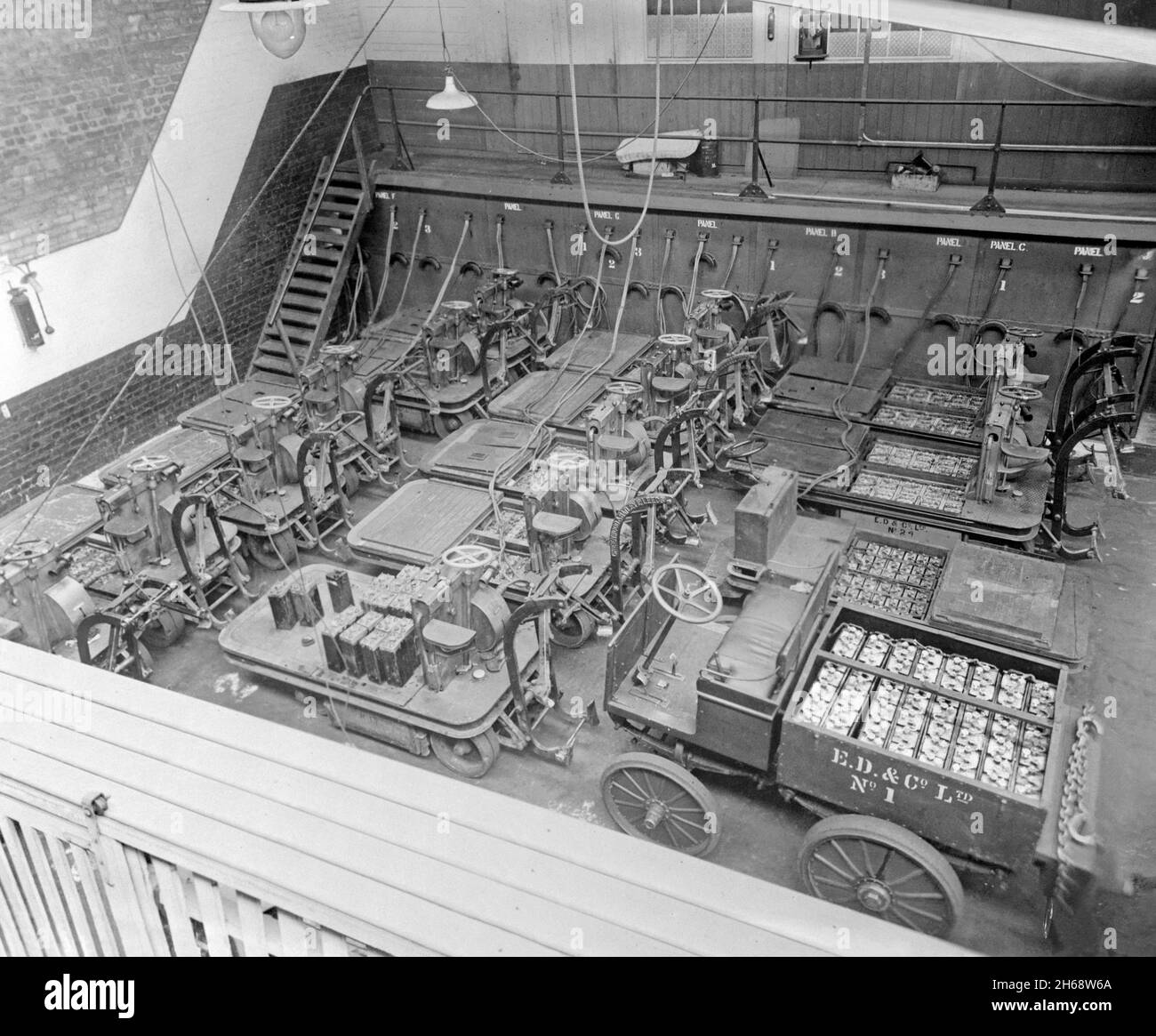 Transport par batterie précoce – ici, les camions et les chariots sont branchés au secteur pour être rechargés la nuit dans un atelier de E D and Co Ltd, une société d'expédition et d'entreposage à Liverpool Docks, Lancashire, Angleterre, Royaume-Uni au début des années 1900.Le grand nombre de batteries nécessaires est évident dans le coin inférieur droit du chariot.Certains chariots sont équipés d'un dispositif de préhension pour déplacer les barils.L’un d’eux (au centre) porte le nom du fabricant en relief – Greenwood et Batley de Leeds.Les premiers véhicules électriques étaient populaires dans les usines, les entrepôts et pour les livraisons locales – une photographie du début du XXe siècle. Banque D'Images Transport par batterie précoce – ici, les camions et les chariots sont branchés au secteur pour être rechargés la nuit dans un atelier de E D and Co Ltd, une société d'expédition et d'entreposage à Liverpool Docks, Lancashire, Angleterre, Royaume-Uni au début des années 1900.Le grand nombre de batteries nécessaires est évident dans le coin inférieur droit du chariot.Certains chariots sont équipés d'un dispositif de préhension pour déplacer les barils.L’un d’eux (au centre) porte le nom du fabricant en relief – Greenwood et Batley de Leeds.Les premiers véhicules électriques étaient populaires dans les usines, les entrepôts et pour les livraisons locales – une photographie du début du XXe siècle. Banque D'Images
