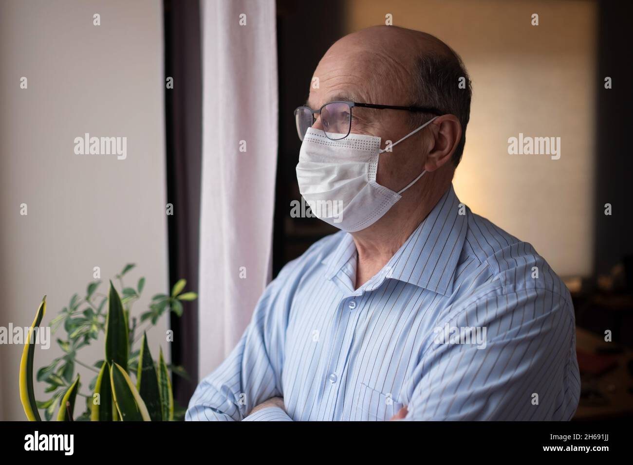 Homme âgé de race blanche portant un masque facial regardant dans la rue près de la fenêtre Banque D'Images