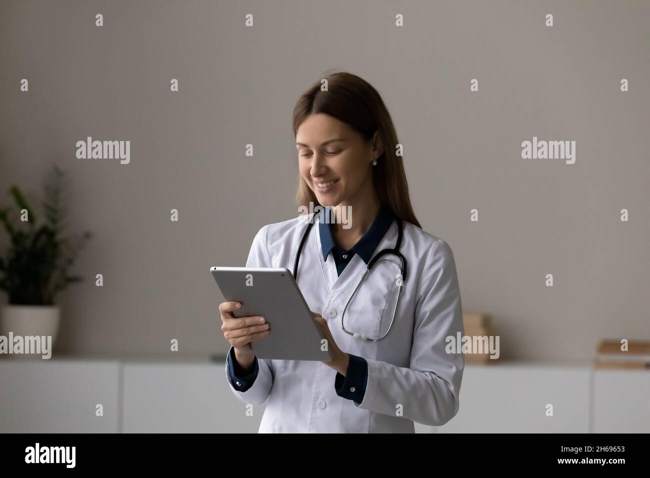Femme souriante médecin thérapeute utilisant une tablette, debout dans la salle de bureau Banque D'Images