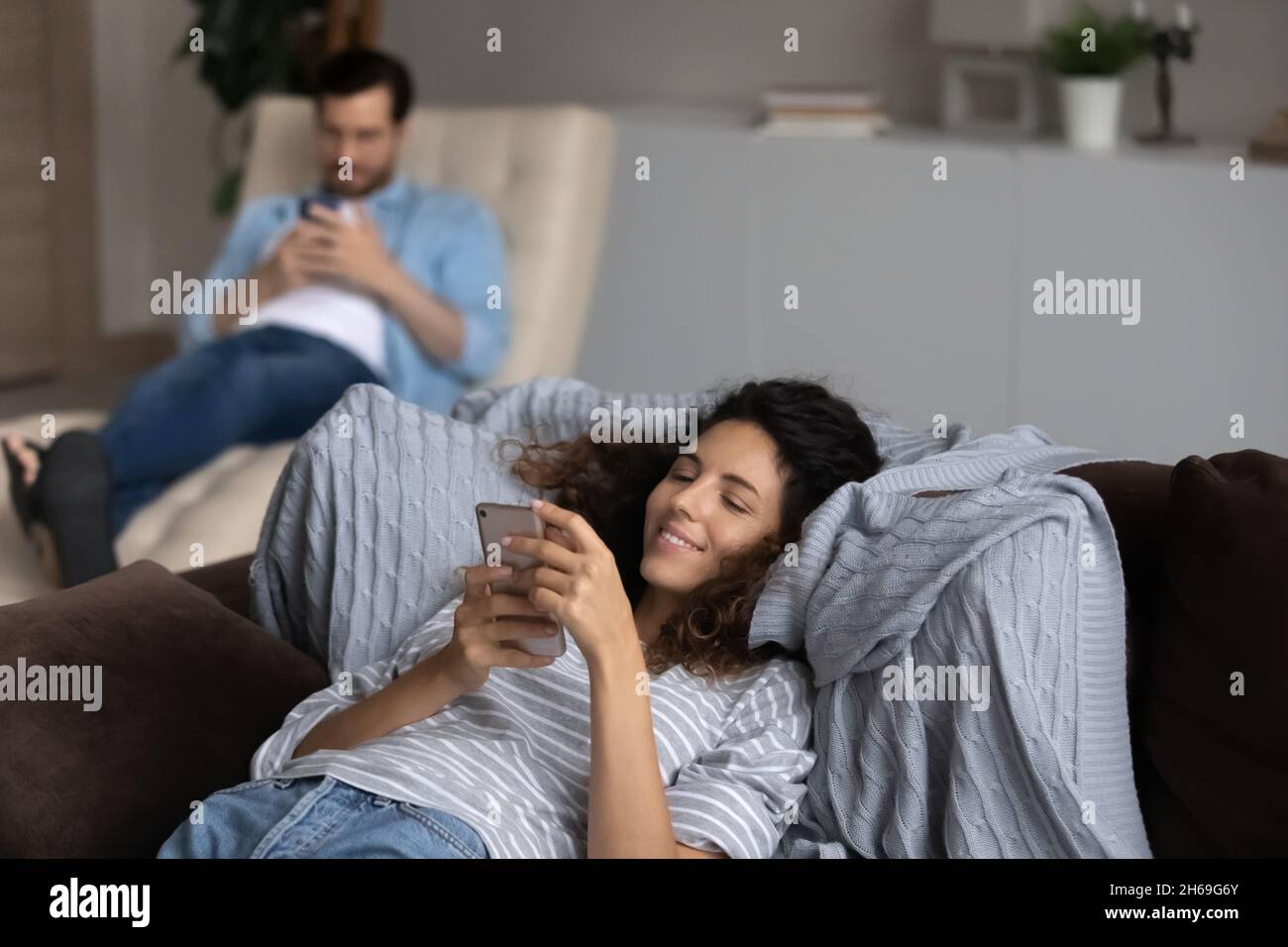 Femme souriante utilisant un smartphone se reposant sur un canapé, couple accro aux appareils Banque D'Images